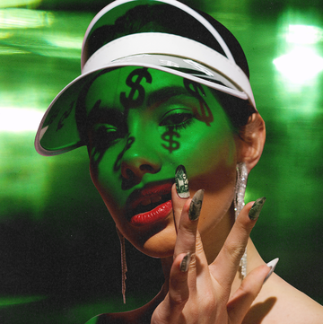 a woman in green light with dollar signs shadowed on her face and dollar bill nail art